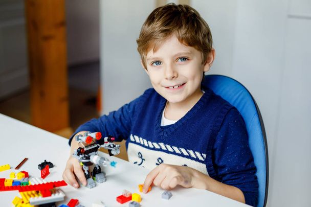 Little blond child playing with lots of colorful plastic blocks. Cute school kid boy having fun with building and creating robot. Creative leisure modern technic and robotic. - Φωτογραφία, εικόνα