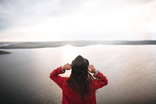 Κορίτσι του ταξιδιώτη με καπέλο και με θυελλώδεις τρίχες που στέκονται στο βράδυ του ήλιου - Φωτογραφία, εικόνα