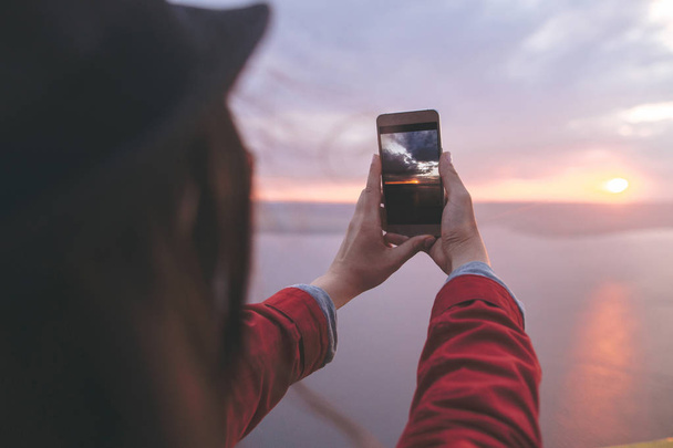 Девушка-путешественница держит телефон и фотографирует прекрасный вечер
 - Фото, изображение