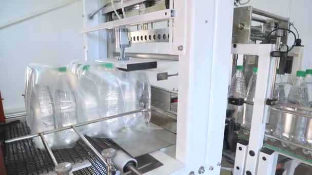 Envase automático de botellas de plástico con película en la prensa de temperatura. Embalaje de botellas para su posterior transporte
. - Imágenes, Vídeo