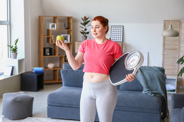 Overweight woman with apple and scales at home. Weight loss concept - Photo, image