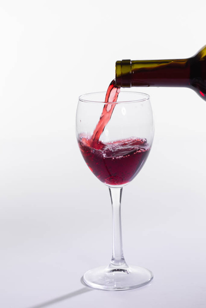 Red wine pouring from bottle into big glass on white background - Photo, Image