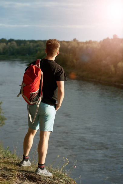 Caucasian young man with red travel backpack standing on the bri - Фото, изображение