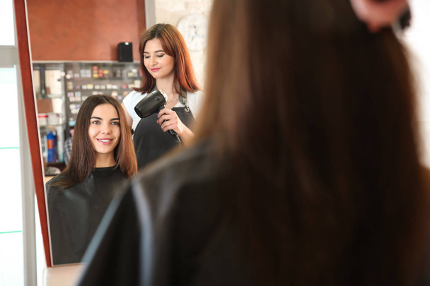 Відбиття жіночого перукаря, що працює з клієнтом в салоні
 - Фото, зображення