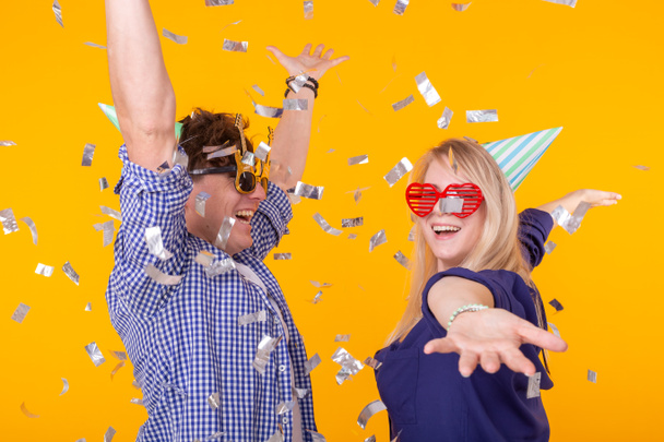 Fun, holidays and party concept - Couple dancing among falling confetti on yellow background - Foto, afbeelding