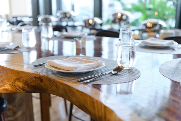 Nastavení tabulky v restauraci. Zdobený elegantní stůl, porcelánové desky, brýle, ubrousek, nůž, vidlička a lžíce na dřevěném stole - Fotografie, Obrázek