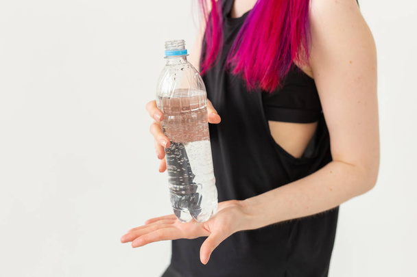Nahaufnahme einer Frau mit farbigem Haar, die eine Flasche Wasser auf weißem Hintergrund mit Kopierraum hält. das Konzept von Durst und Wasserhaushalt des Körpers. - Foto, Bild