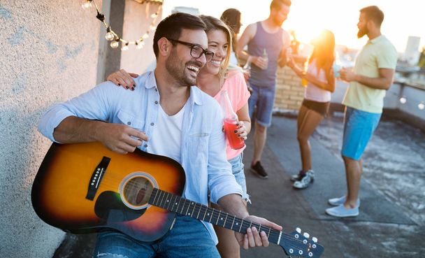 Jonge vrienden die plezier hebben op een dakfeest, gitaar spelen, zingen, dansen en chillen - Foto, afbeelding