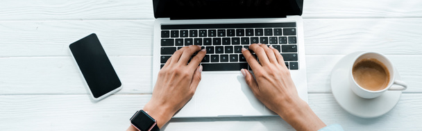 panoraama laukaus naisen kirjoittamalla kannettavan tietokoneen lähellä älypuhelimen ja kupin kahvia
  - Valokuva, kuva