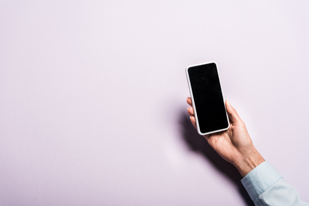 обрезанный вид женщины, держащей смартфон с пустым экраном на фиолетовом
 - Фото, изображение