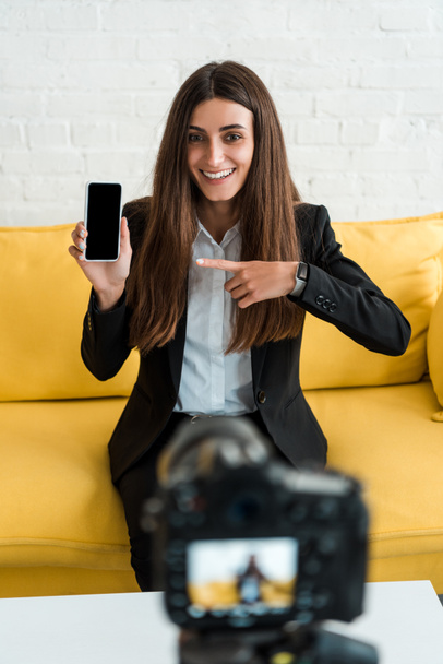 foyer sélectif de la femme heureuse pointant du doigt le smartphone avec écran vide près de l'appareil photo numérique
  - Photo, image