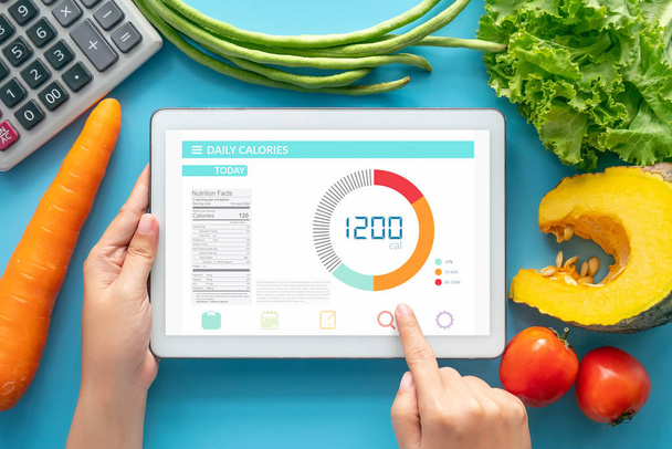 Calories counting , diet , food control and weight loss concept. woman using Calorie counter application on tablet at dining table with fresh vegetable and calculator - Fotoğraf, Görsel