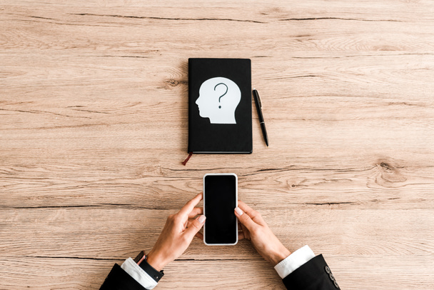 top view of woman holding smartphone with blank screen near notebook and paper human head with question mark  - Photo, Image