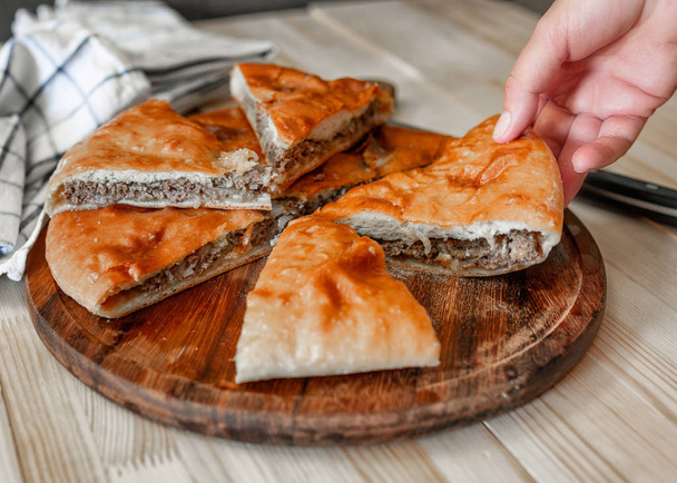 Pasteles tradicionales de carne de Osetia con carne de res con una mano femenina
 - Foto, imagen
