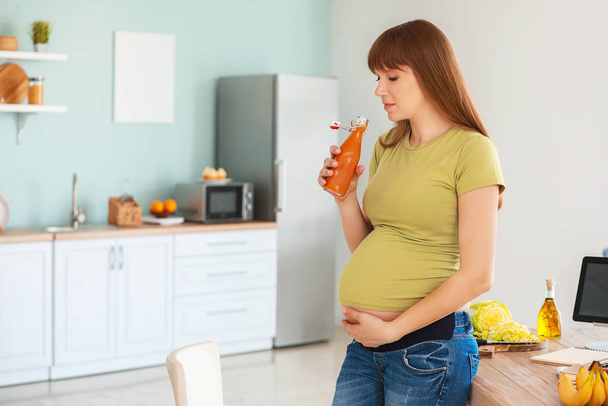 Beautiful pregnant woman drinking juice in kitchen - Foto, Imagem