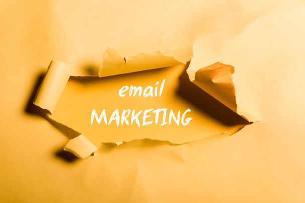 tattered paper with email marketing lettering and rolled edges on orange - Photo, Image