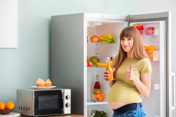 Schöne schwangere Frau nimmt Saft aus Kühlschrank in Küche - Foto, Bild