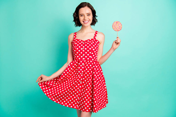 Pretty lady holding big candy on stick wear red dotted dress isolated teal background - Φωτογραφία, εικόνα