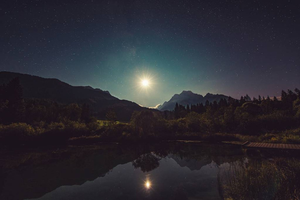 Beautiful glowing moon with its reflection in a lake with hills and shiningstars - Zdjęcie, obraz