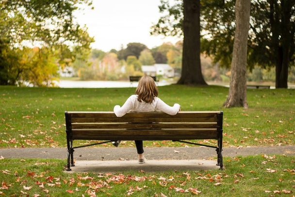 Feminino sentado em um banco em um parque tiro de trás na queda com um lago no fundo
 - Foto, Imagem