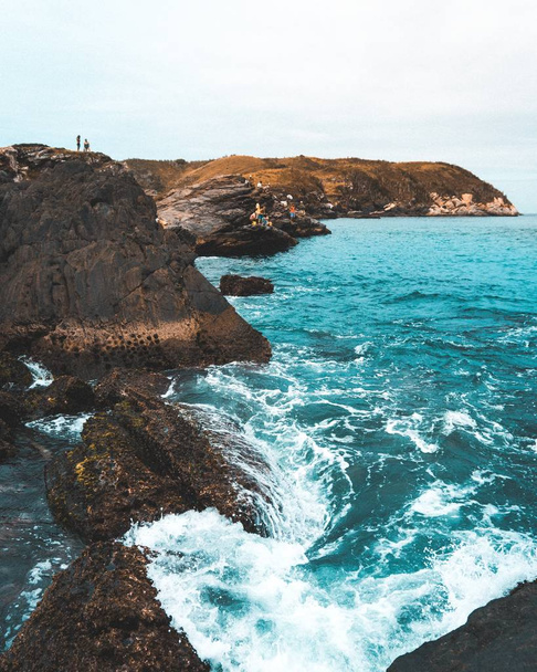Beautiful ocean waves hitting rocks near the coast with people standing on rocks - Φωτογραφία, εικόνα