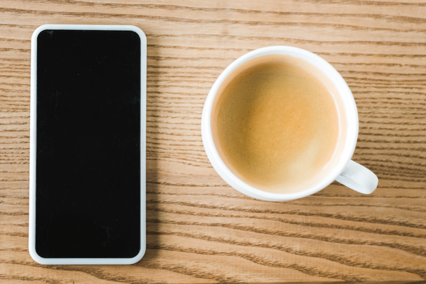 top view of smartphone with blank screen near cup of coffee on table  - Photo, Image