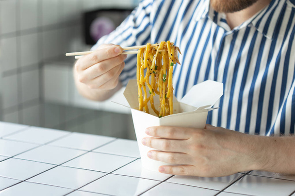 El primer plano de una joven mano de hombre no identificado en una camisa sostiene palos de madera fideos chinos. Deliciosa cocina asiática concepto
. - Foto, imagen