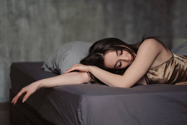 Kaunis seksikäs brunette nainen makaa sängyllä. Kasvot lähikuva, kauniit ruskeat silmät, huulet ja hymy
. - Valokuva, kuva