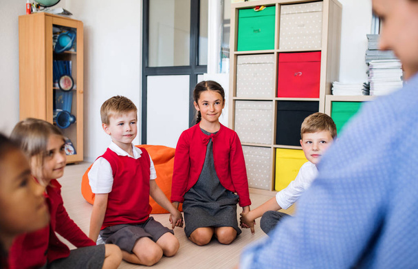 Um grupo de crianças de escola pequena com professor sentado no chão em classe, de mãos dadas
. - Foto, Imagem