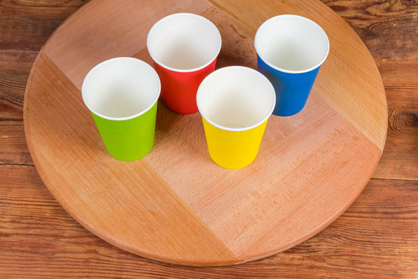Bicchieri di carta usa e getta in diversi colori su tavola da portata in legno
 - Foto, immagini