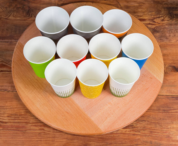 Diferentes vasos de papel desechables vacíos en el tablero de servir de madera
 - Foto, Imagen
