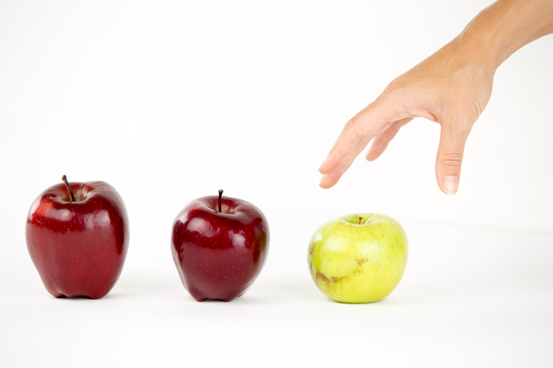 Pojem rozmanitosti: ženská ruka se chystá chytit jediné zelené jablko mezi ostatními červenými - Fotografie, Obrázek