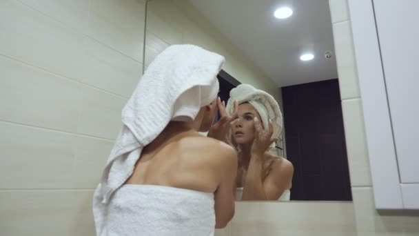 Νεαρή γυναίκα κοιτάζοντας καθρέφτη και αγγίζοντας το πρόσωπο μετά το πρωί ντους. - Πλάνα, βίντεο