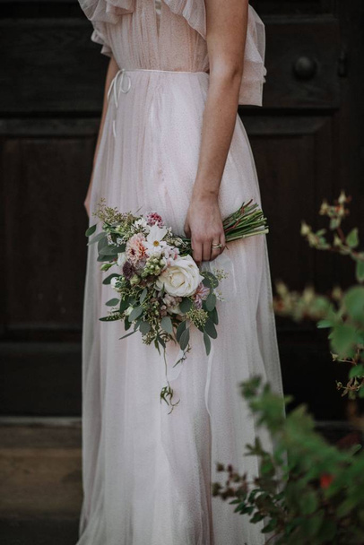 Vertical shot of a bride wearing wedding dress holding a flower bouquet - Foto, immagini