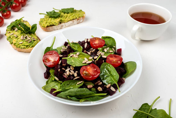 Healthy vegetarian food. Salad with beetroot, spinach, cherry tomatoes and seeds. - Photo, Image