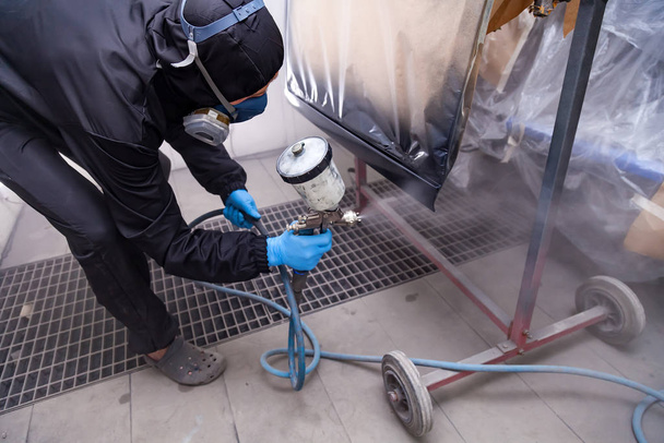 A male worker in jumpsuit and blue gloves paints with a spray gu - Foto, Imagen