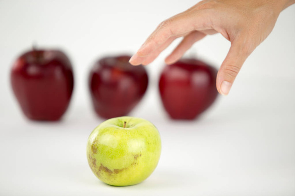Concept of diversity: a woman's hand is about to grab the only green apple among the other red ones - Photo, Image