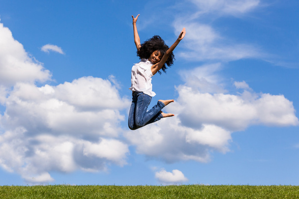 Outdoor portrait of a teenage black girl jumping over a blue sky - Фото, изображение
