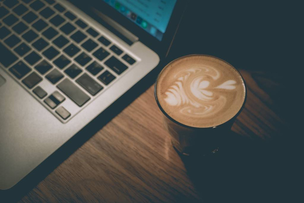 A cup of well-made latte next to a laptop - Foto, Imagem