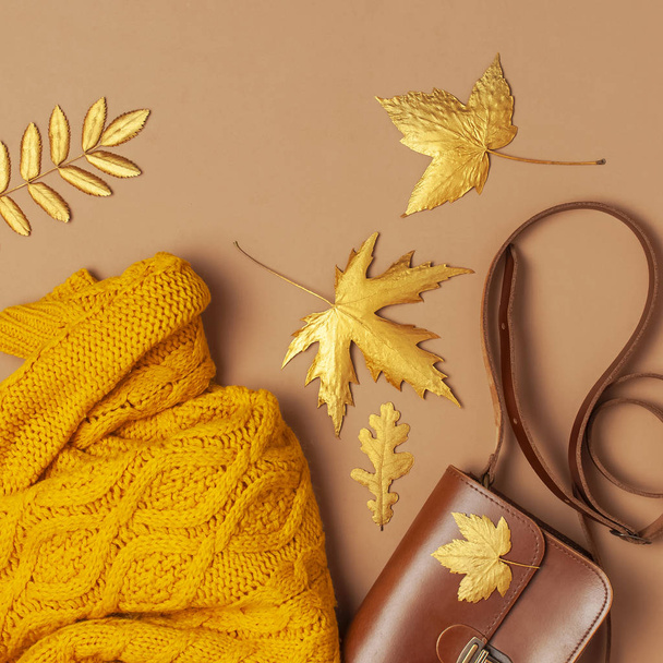 Женская сумка из коричневой кожи, оранжевый вязаный свитер, золотой осенний лист на коричневом фоне. Модные женские аксессуары. Осенняя концепция моды. Стильная женская одежда
 - Фото, изображение