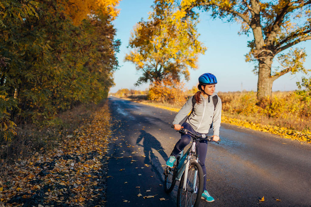 Young bicyclist riding on autumn field road at sunset. Happy woman traveler smiling - Photo, Image