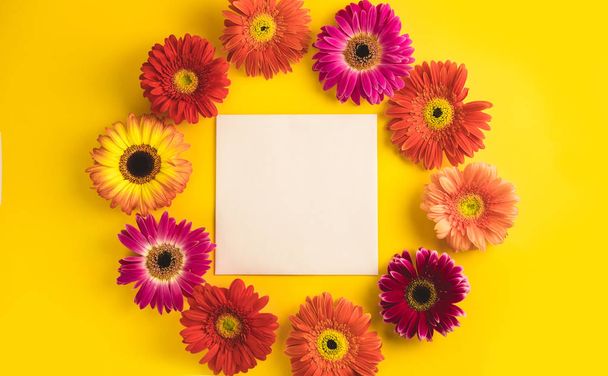 Bright beautiful gerbera flowers and paper card on a sunny yellow background. Mothers Day, Valentine holiday. Place for text, lettering or product. View from above, Copy space. Flatlay. - Zdjęcie, obraz