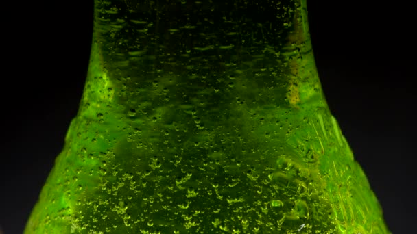 HD. kondenzációs csepp gurul egy szóda palack. Gázbuborékok a palackon belül. Egy fekete háttér üveg zöld szóda. Nedves. - Felvétel, videó