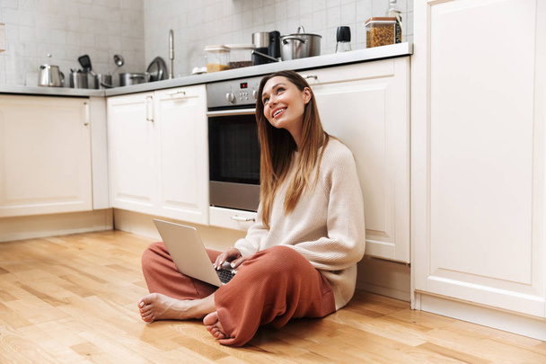 Cheerful young girl sitting on a floor at the kitchen - Photo, image