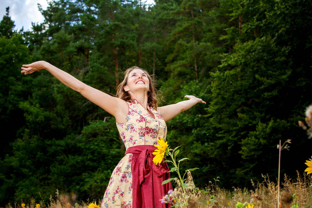 mulher em dirndl de pé no campo das flores e espalhando-lhe um
 - Foto, Imagem