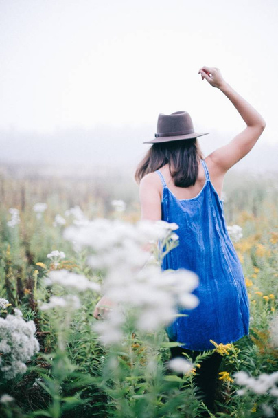 Woman in a hat and a blue long dress walking in a beautiful flower field - Valokuva, kuva