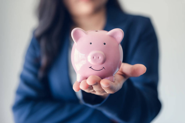 Business Woman befektetői Holding Piggy Bank pénz megtakarítás a kezét, ázsiai üzletasszony az egységes suit megjelenítve pénz mentése miközben nézi Camera., beruházás és pénzügyi koncepció. - Fotó, kép