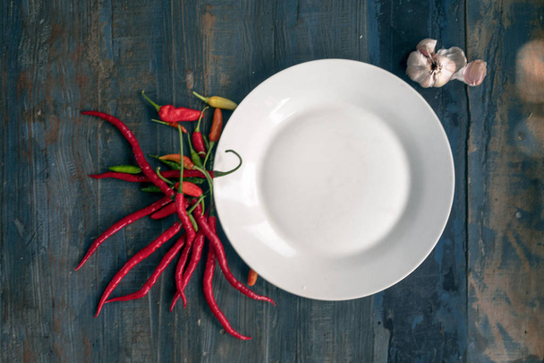 white plate on the background of old boards, wood, with chili pepper, spices - Photo, image