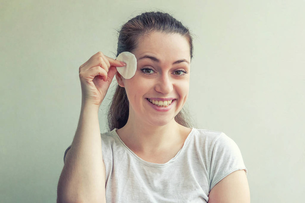 Yumuşak sağlıklı cilt kaldırarak gülümseyen kadın beyaz arka plan üzerinde izole pamuk ped ile makyaj - Fotoğraf, Görsel