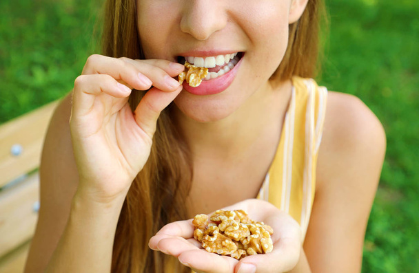 Крупным планом молодая женщина ест грецкие орехи в парке
. - Фото, изображение